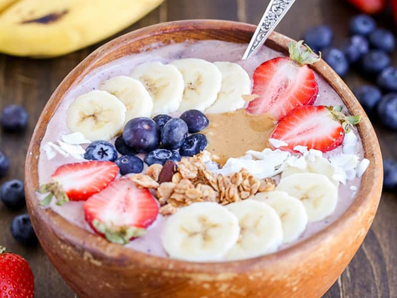 Acai bowl topped with sliced bananas and strawberries, blueberries, granola and a dollop of peanut butter.