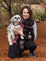 Author Stacy Covitz in exercise clothes standing on top of a mountain holding a dog