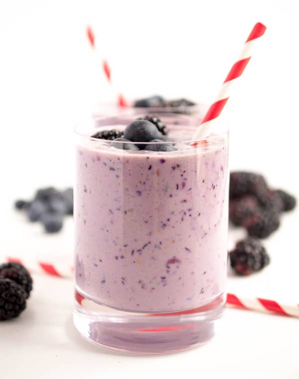 Purple smoothie with blueberries and blackberries on top. Red and white striped straw is sticking out of glass.