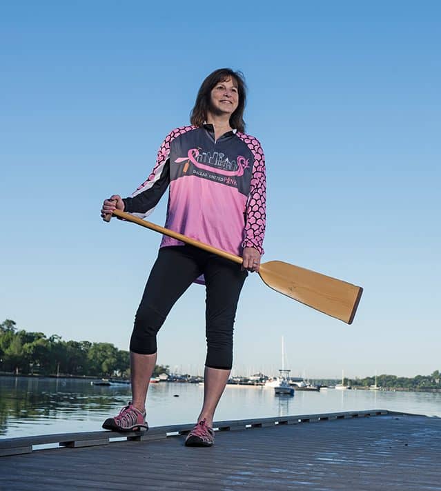 Breast cancer survivor Kathy Bockman stands on dock with paddle for dragon boat racing.