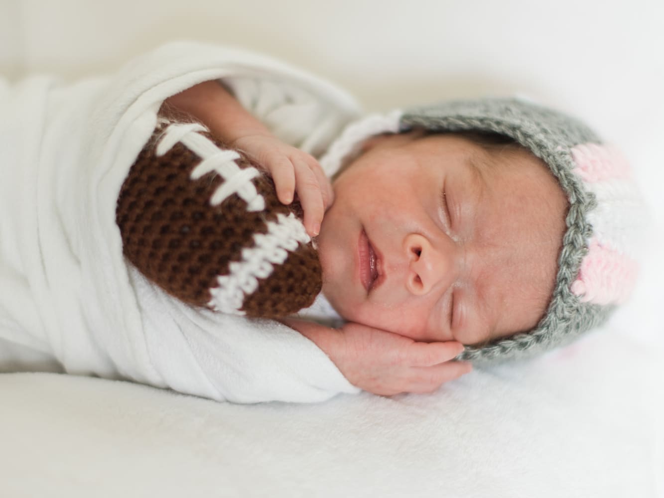 Baby in the NICU wearing a crochet football helmet.