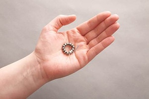 LINX implant in the palm of a hand; it's about the size of a quarter.