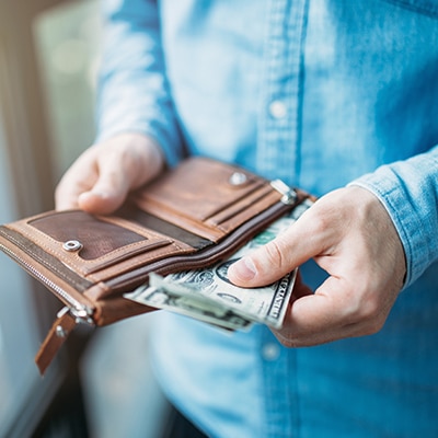 Person wearing jean button down taking out two cash bills from brown leather wallet