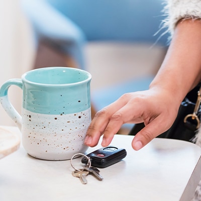 Woman reaching for car and house keys resting on table next to aquamarine and white mug